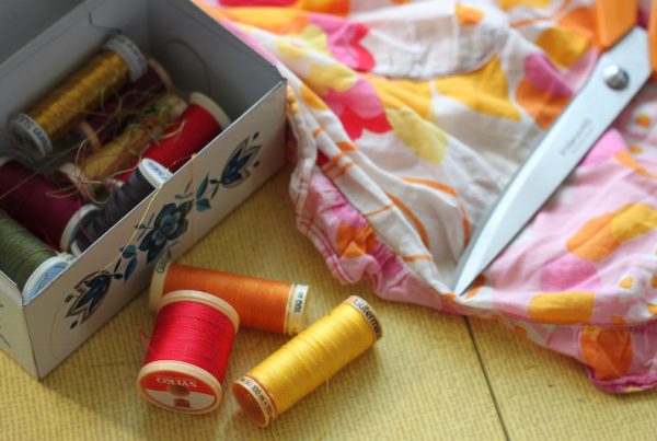 A tin of cotton reels, scissors and fabric